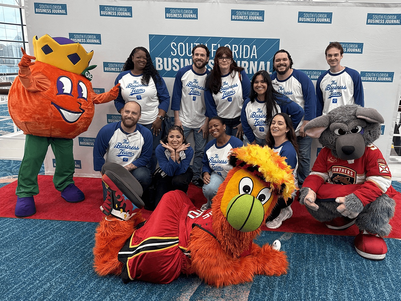 iBusiness employees in matching team shirts pose with sports mascots at a South Florida Business Journal event