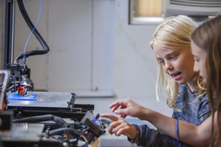 Two children examine a 3D printer during an iCAMP activity