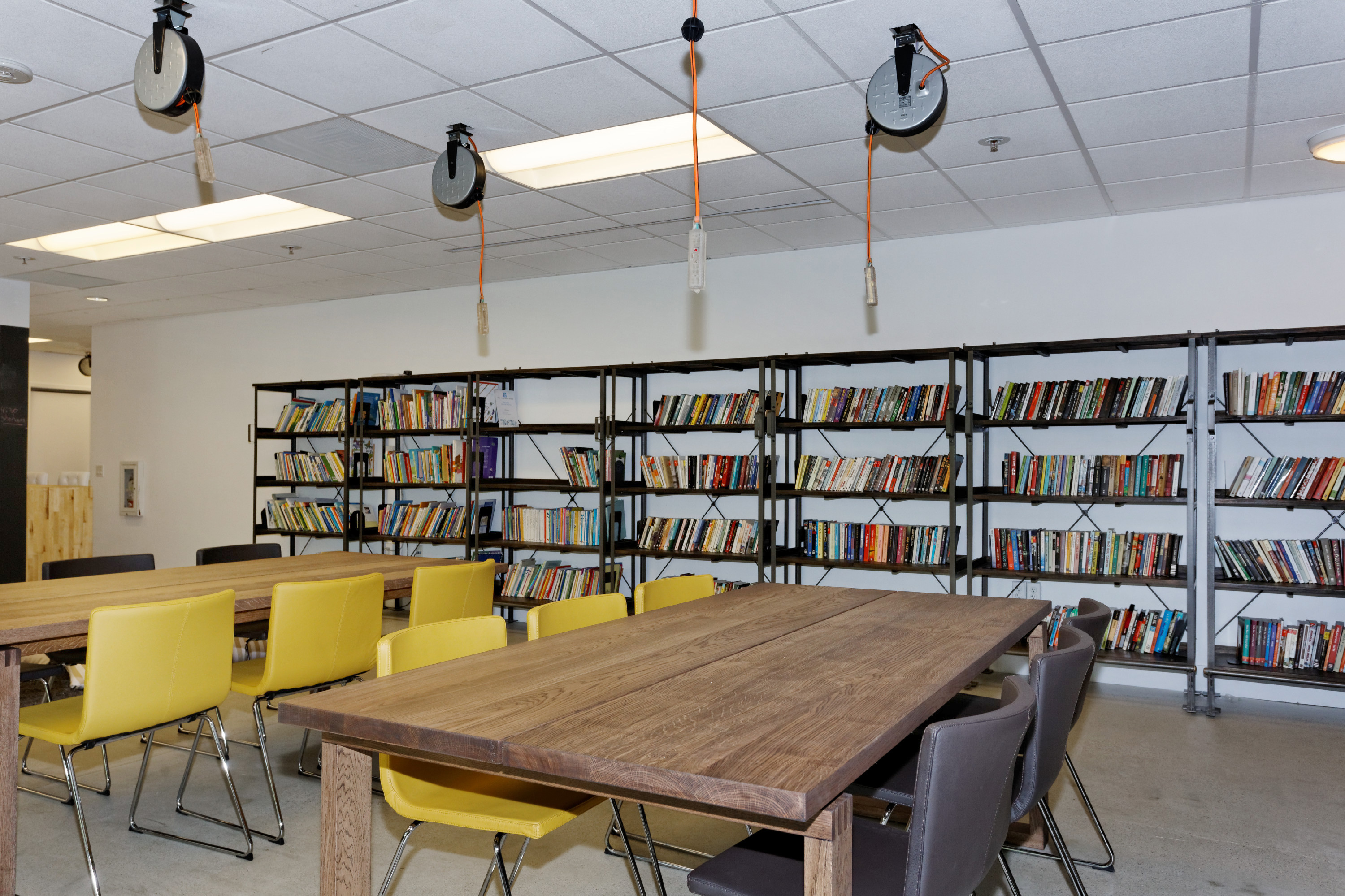 ICON workspace with shared wooden tables, yellow chairs and bookshelves
