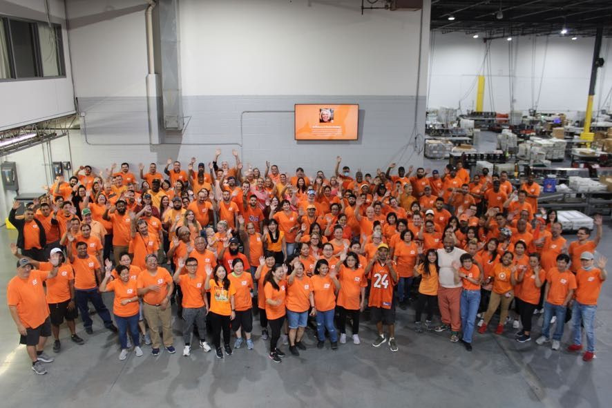 ICS employees gathered in orange shirts on the factory floor