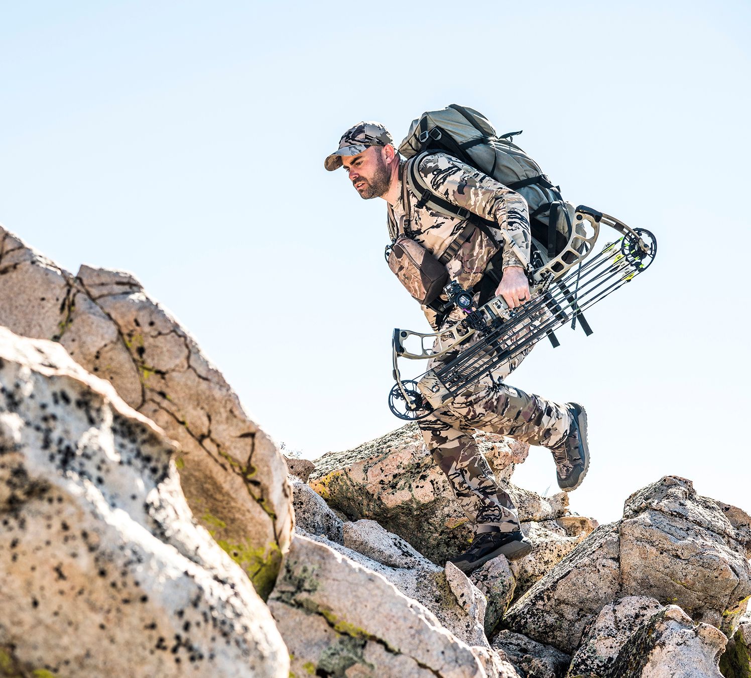 A bowhunter climbs through a rocky landscape in an outdoor campaign photograph