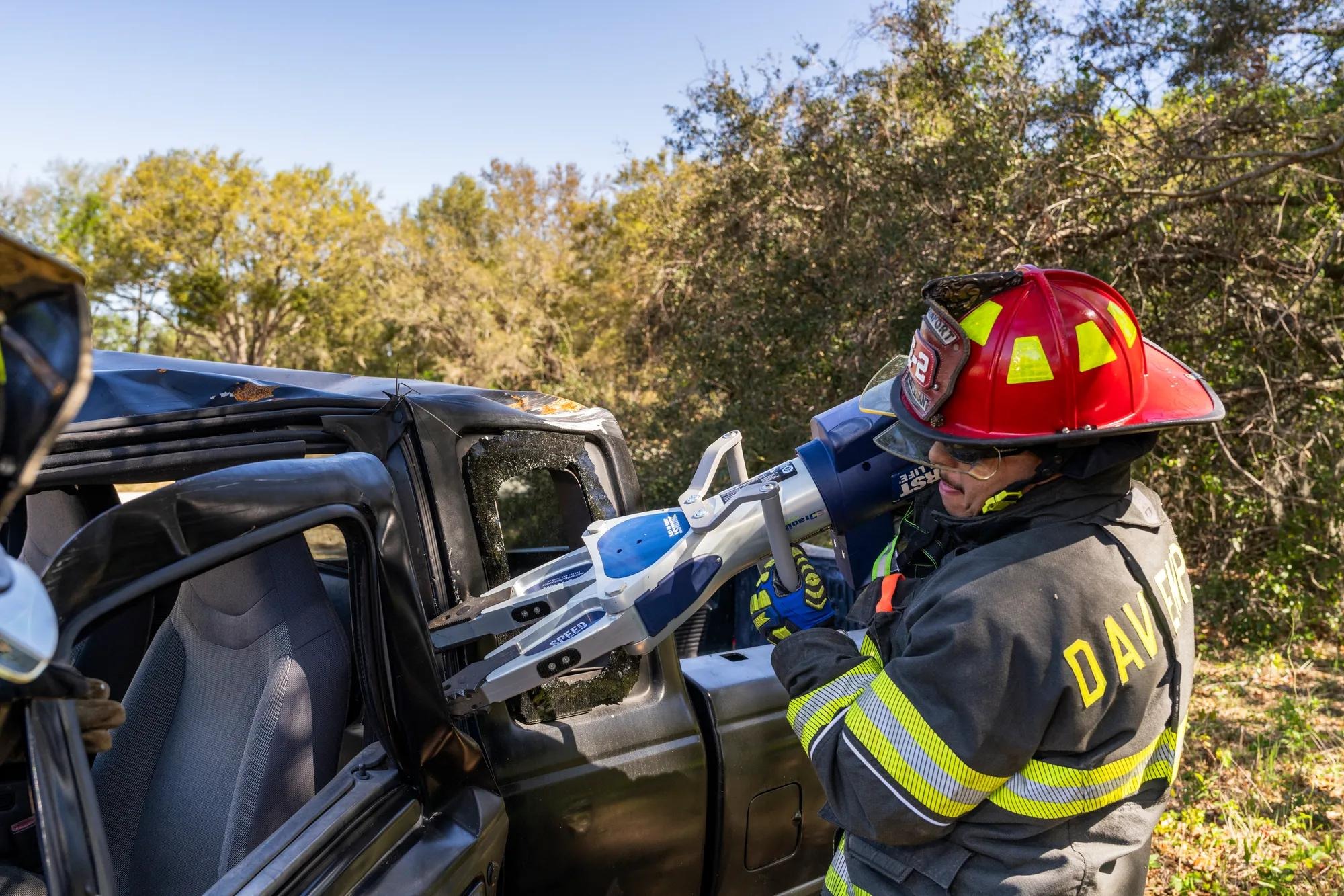 A firefighter operates a blue and white HURST spreader against a damaged vehicle
