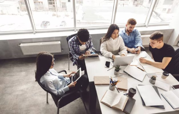 Five people working with laptops and tablets around a meeting table