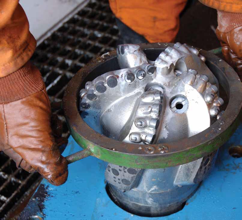 Gloved hands handling a metal drill bit, photographed for an IHS upstream-energy brochure