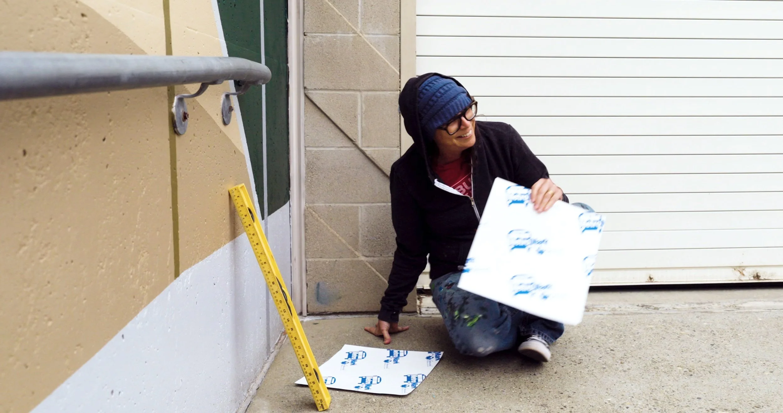 Missy Reitner-Cameron kneels beside a wall with a measuring level and materials
