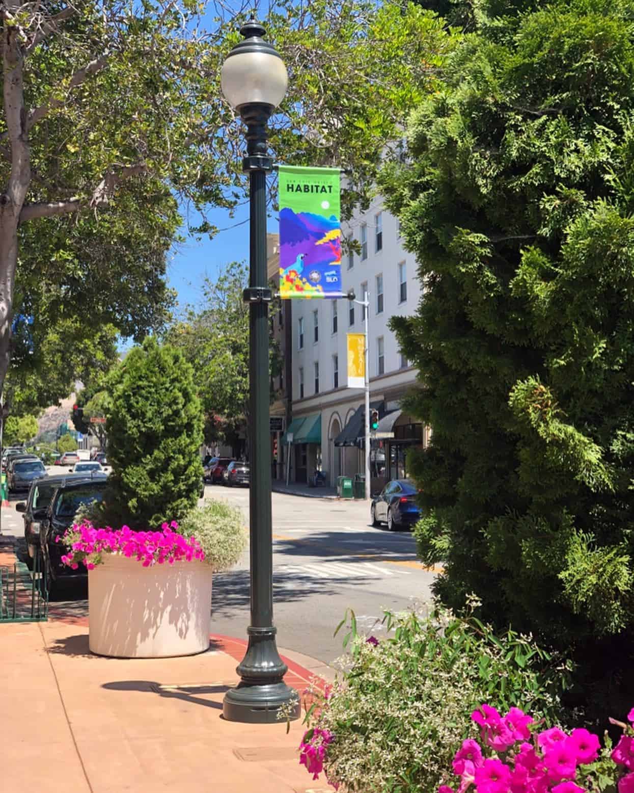 A colorful Habitat banner designed by iii DESIGN hangs from a downtown San Luis Obispo light pole