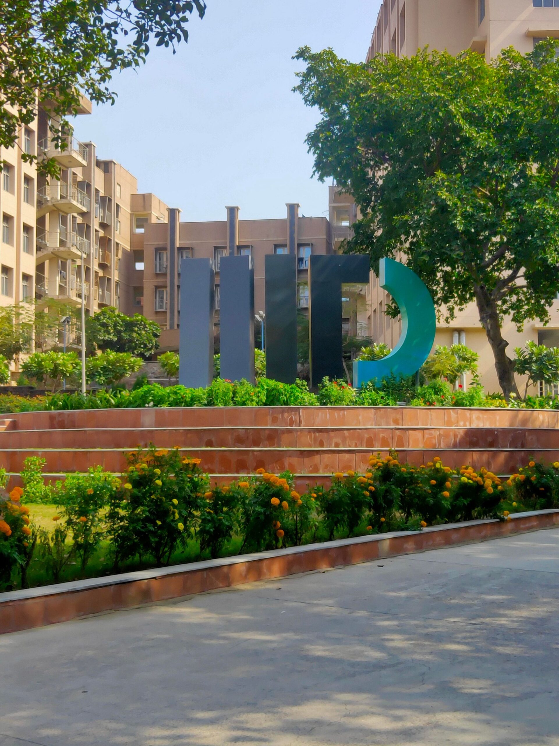 IIIT Delhi campus courtyard with trees and a large IIITD installation