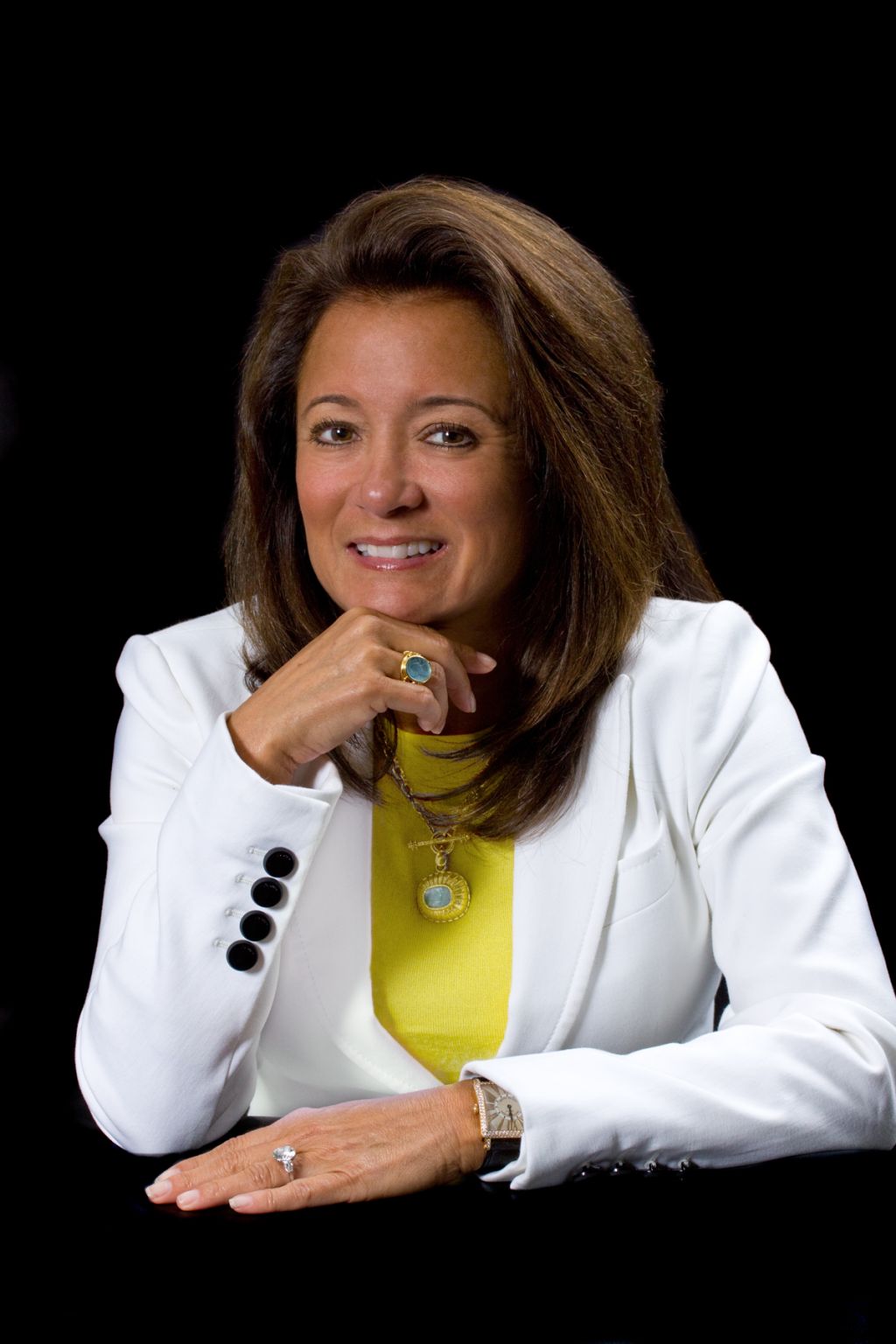 Ileana Quintas seated against a black background in a white jacket and yellow top