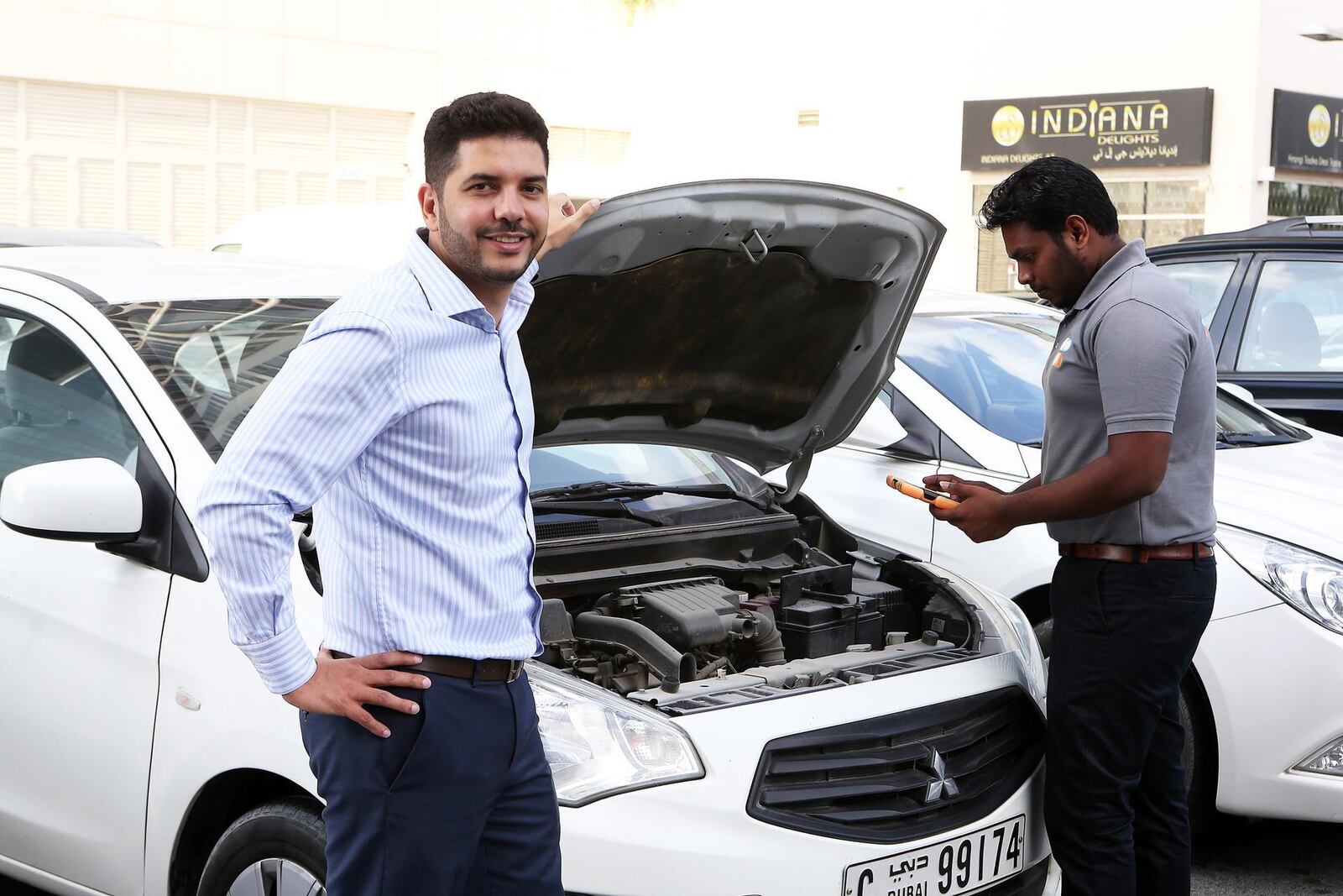 Imad Hammad beside a white car with its bonnet open as a mechanic examines the engine