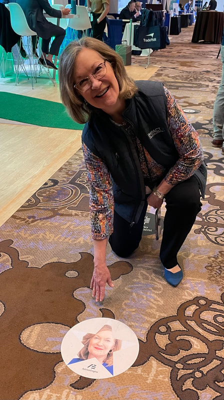 Marie Swift smiling at a 2024 financial technology conference beside a floor marker printed with her portrait