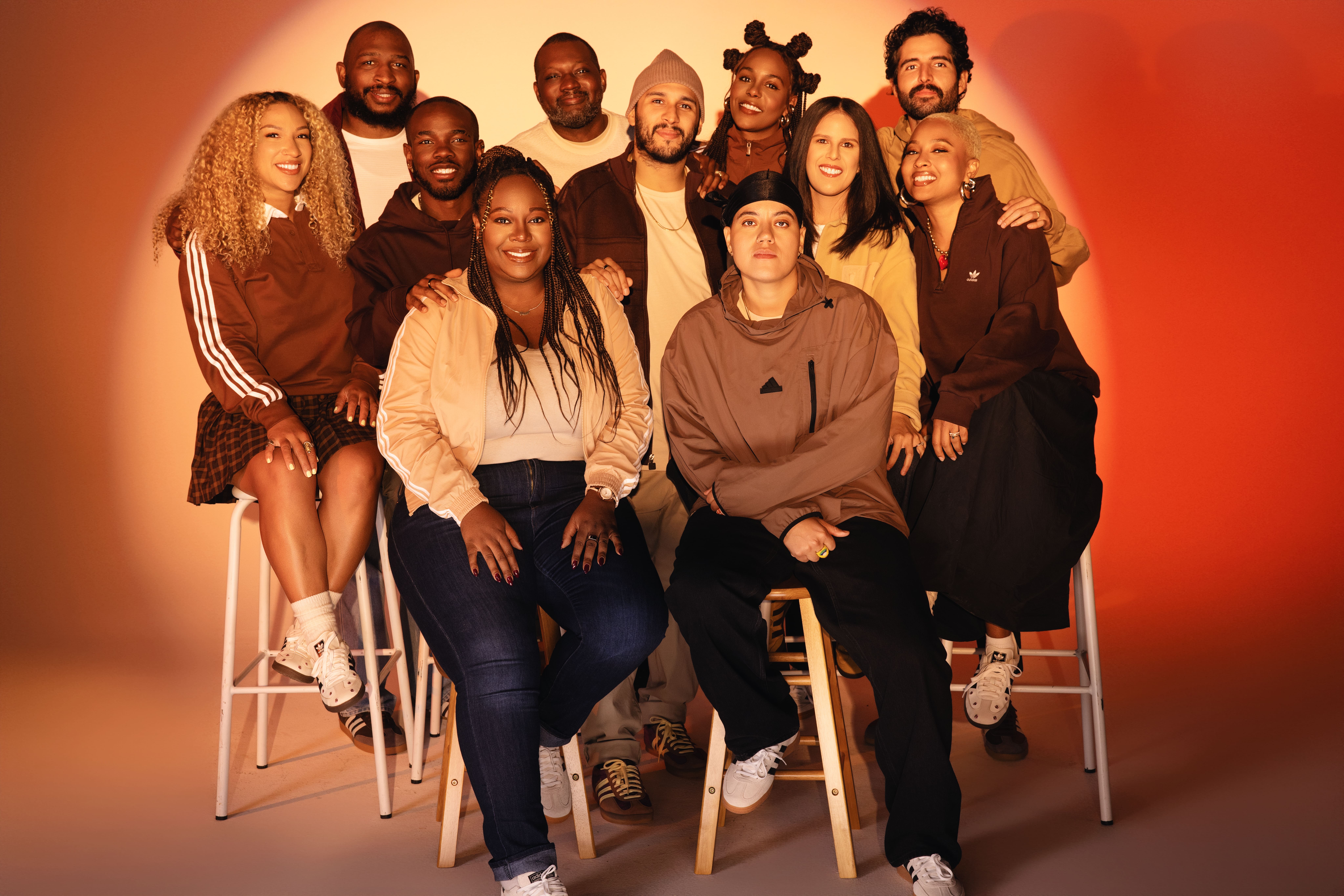 The adidas Community Lab 2024 cohort poses together in an orange-lit studio.