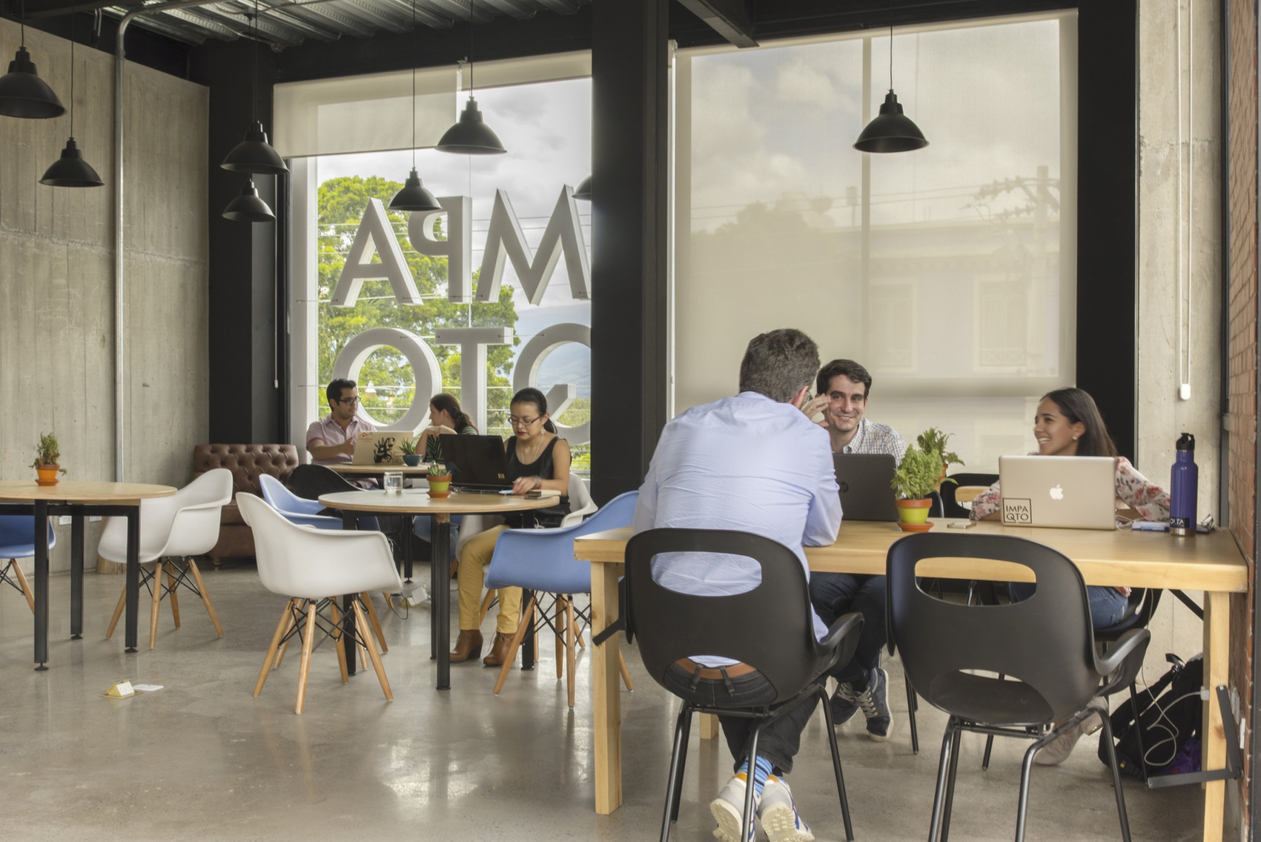 People working and talking at shared tables in an IMPAQTO workspace