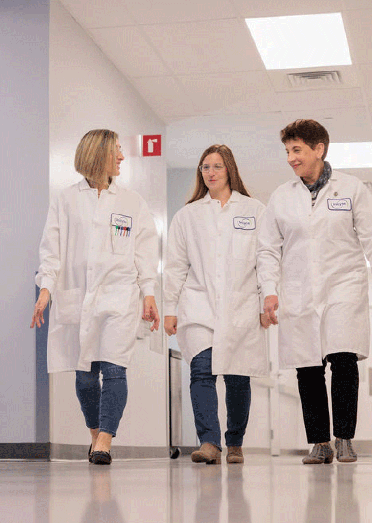 Scientific professionals in lab coats walking through an Incyte research-facility corridor