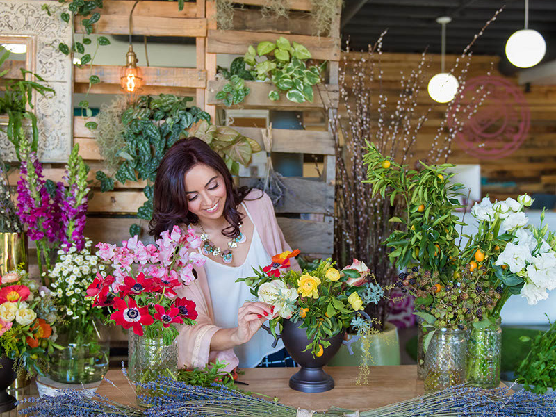 A woman arranging flowers among vases and greenery in a BloomNation portfolio photograph