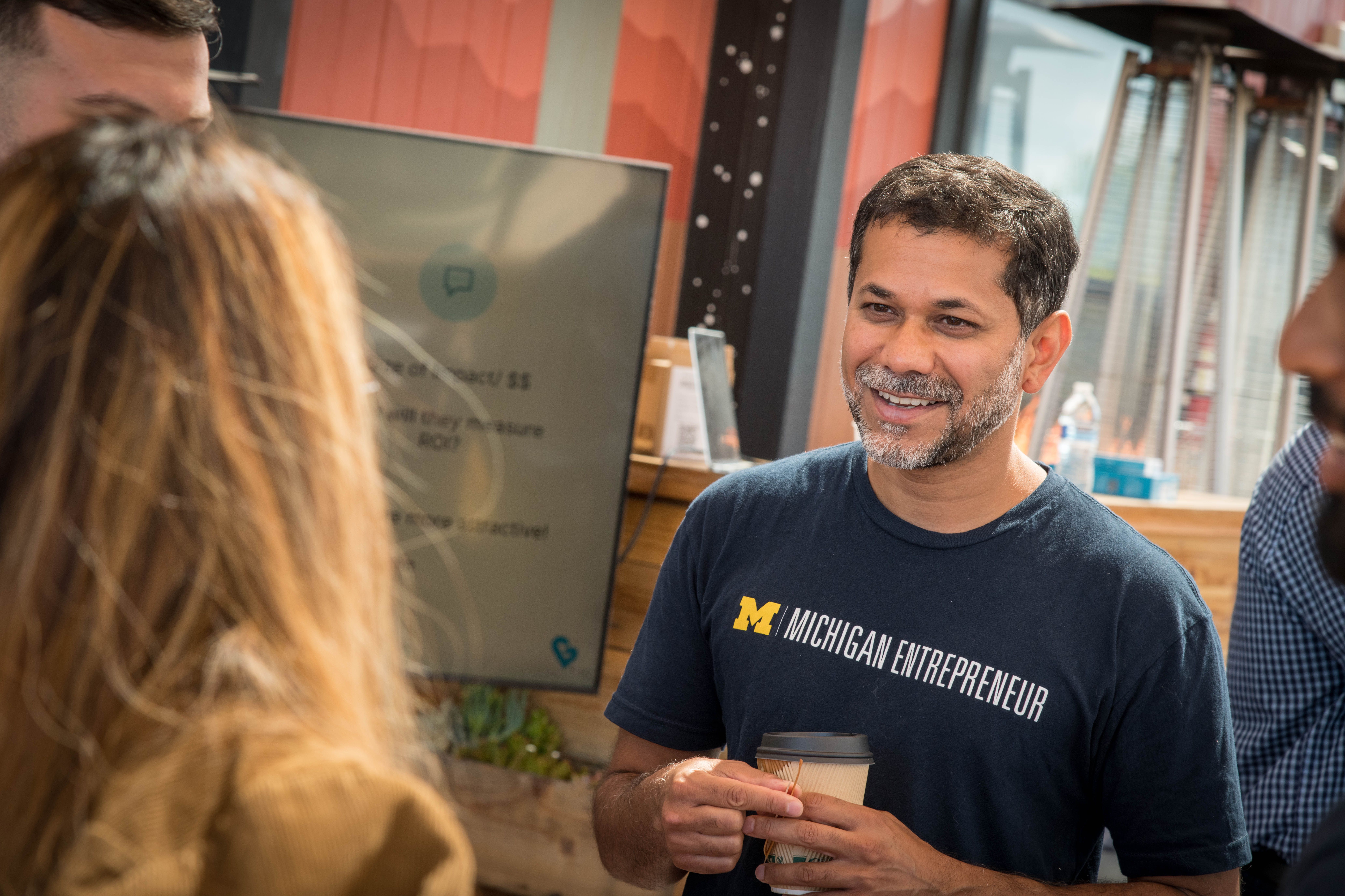Inder Singh holding a coffee cup and speaking with Michigan students during an entrepreneurship trek