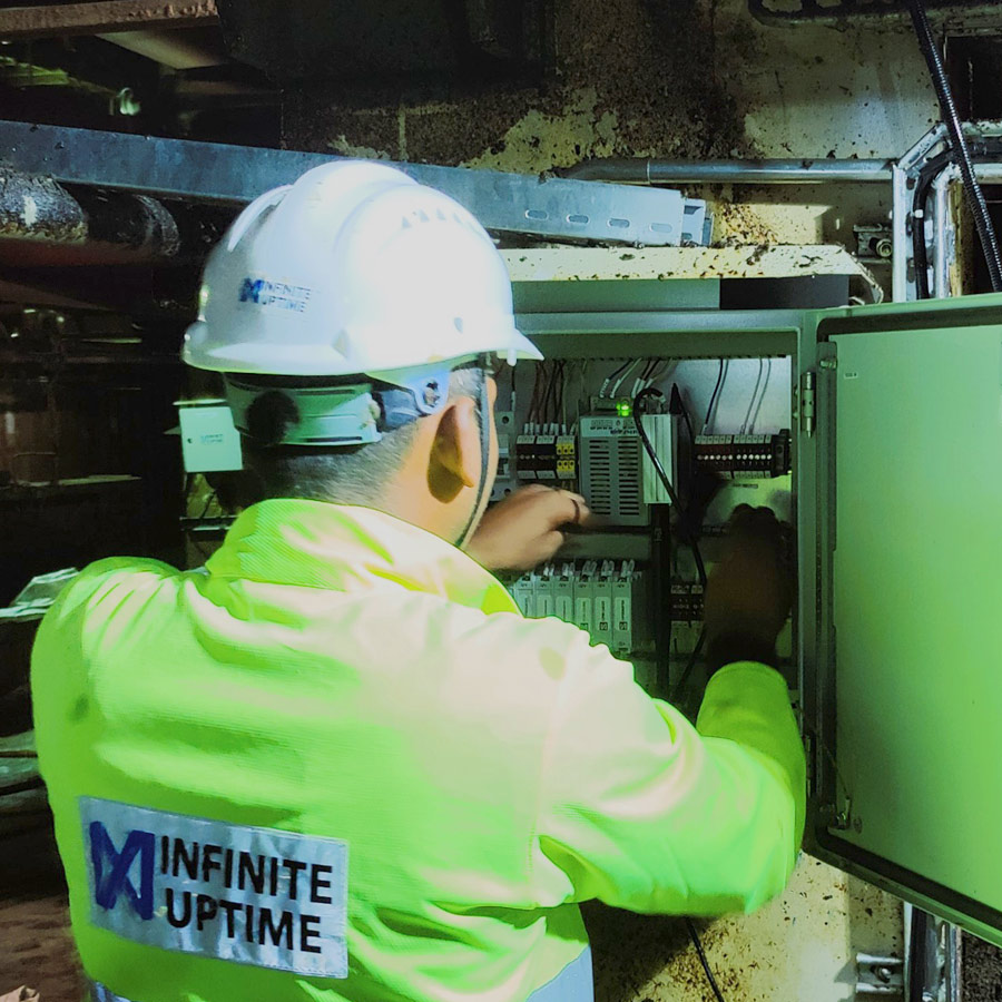 An Infinite Uptime technician working inside an industrial control cabinet