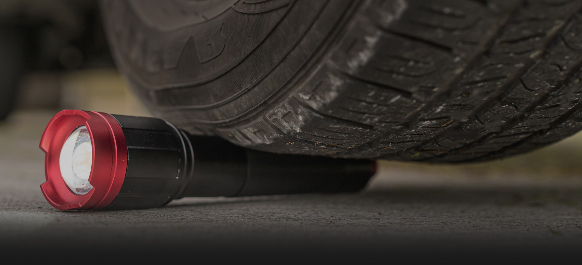 An Infinity X1 hybrid flashlight lying on pavement beside a vehicle tire