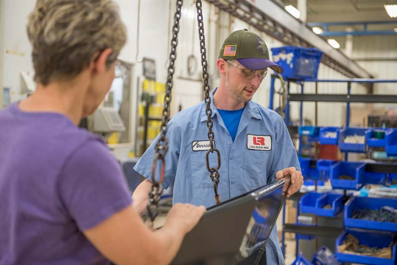 Two Lou-Rich workers handling a suspended metal component