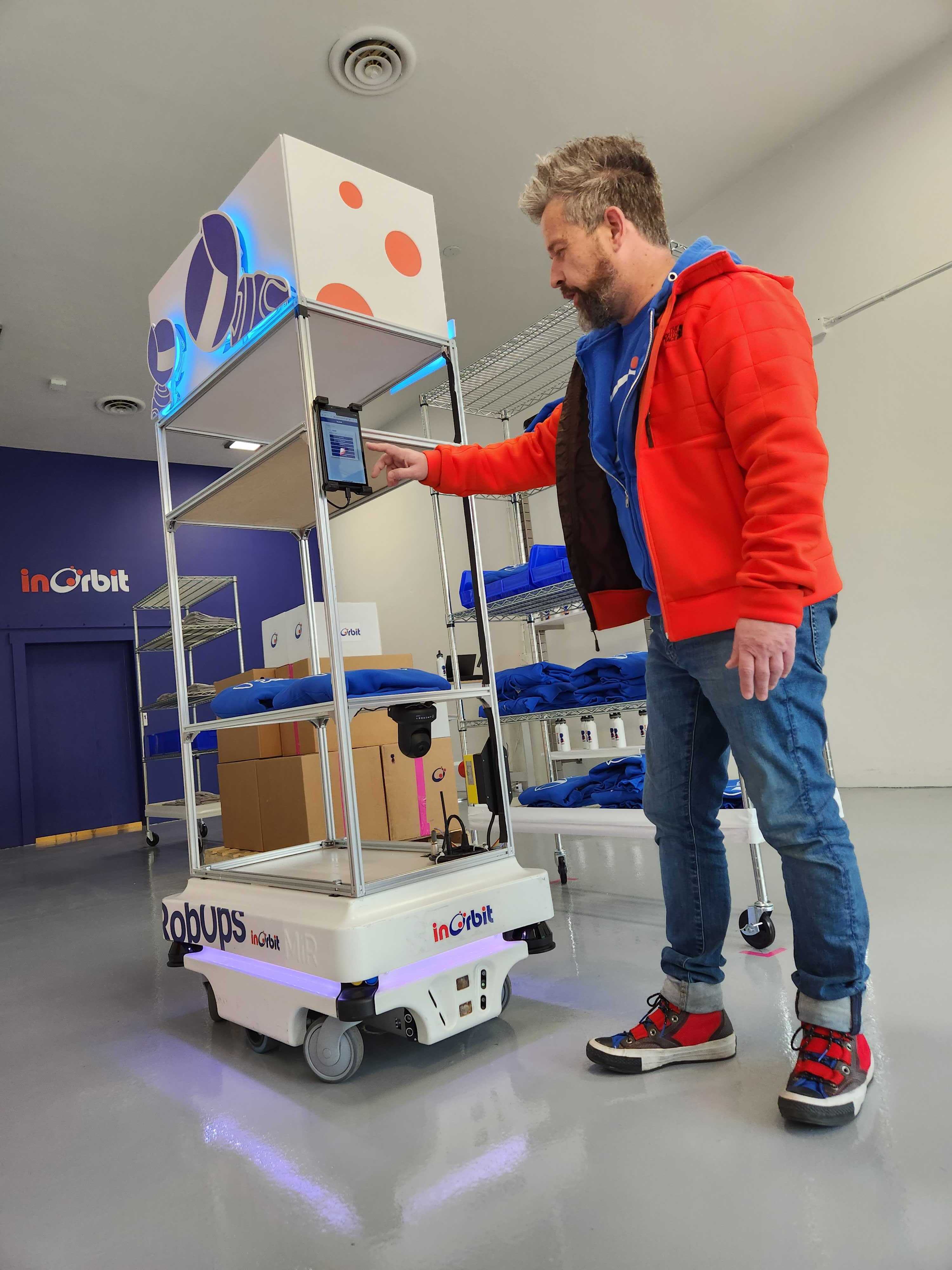 A person uses the mounted screen on a mobile shelving robot at InOrbit Robot Space