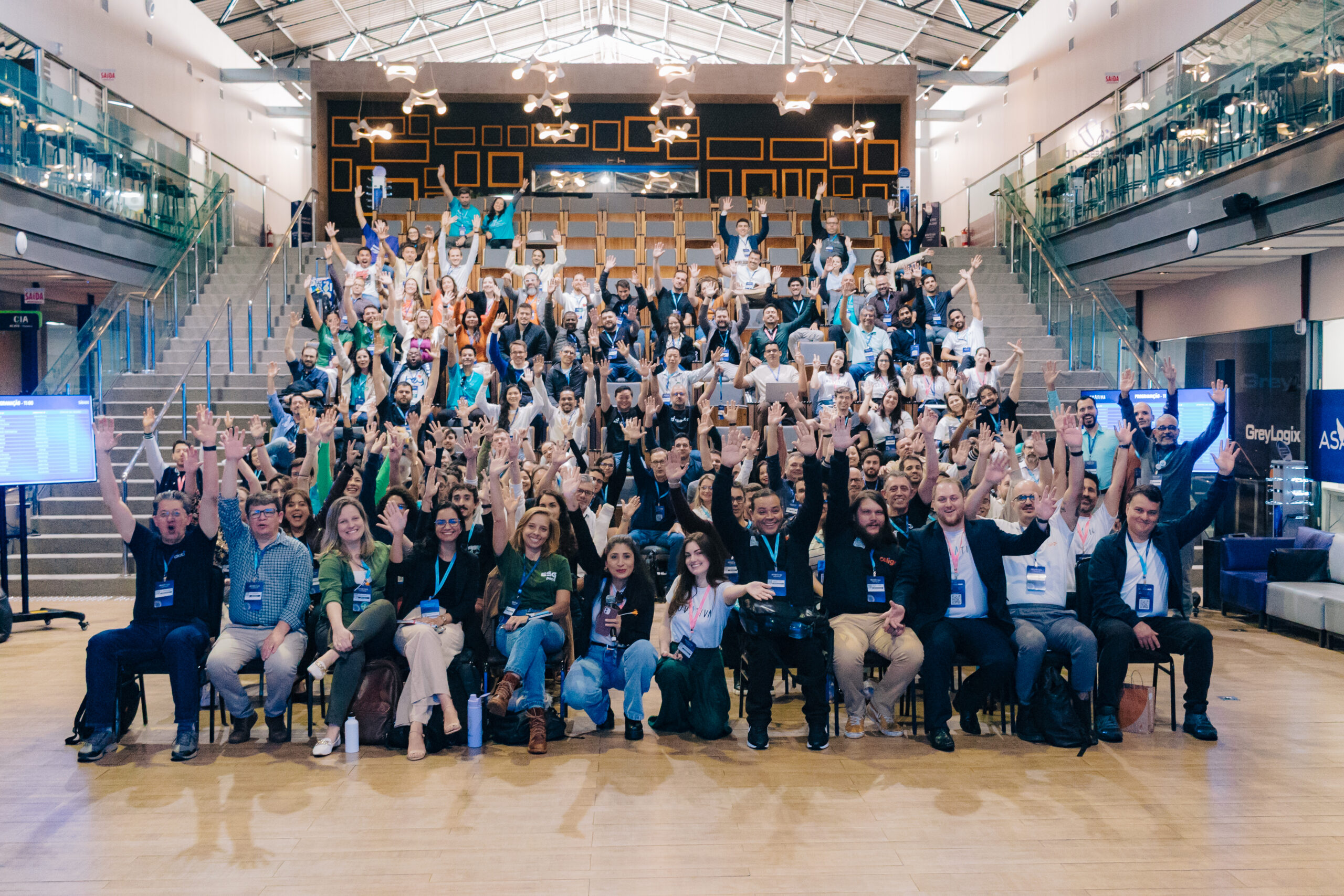 InovAtiva Experience participants wave from tiered seating in a bright event space