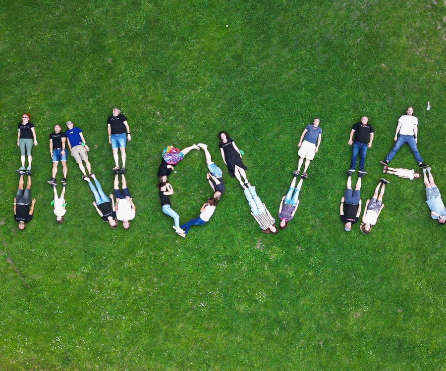 INOVIA team members lie on a lawn, arranging themselves into the letters of the organisation’s name