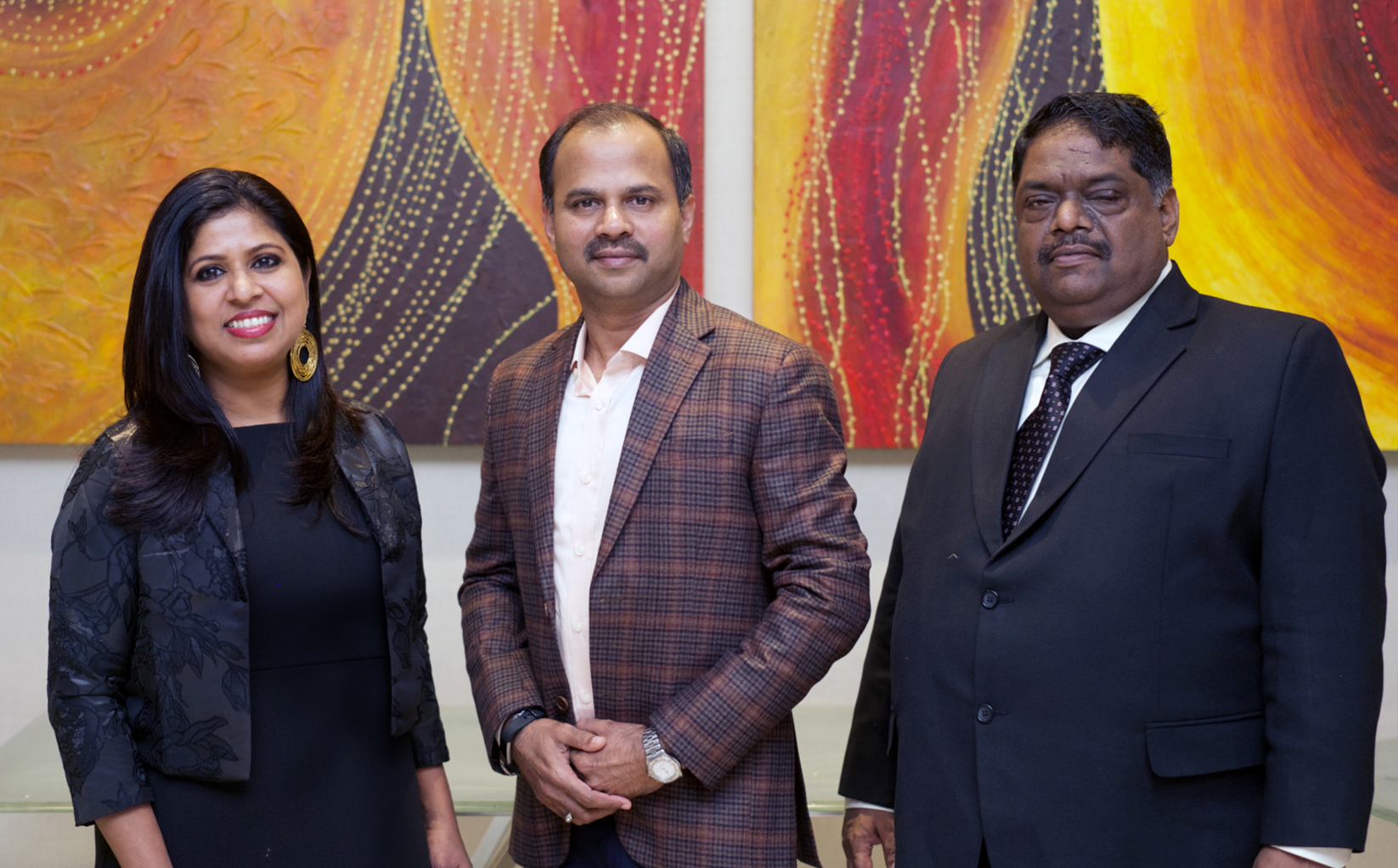 Three members of Inscribe Graphics’ leadership posing in front of colorful artwork