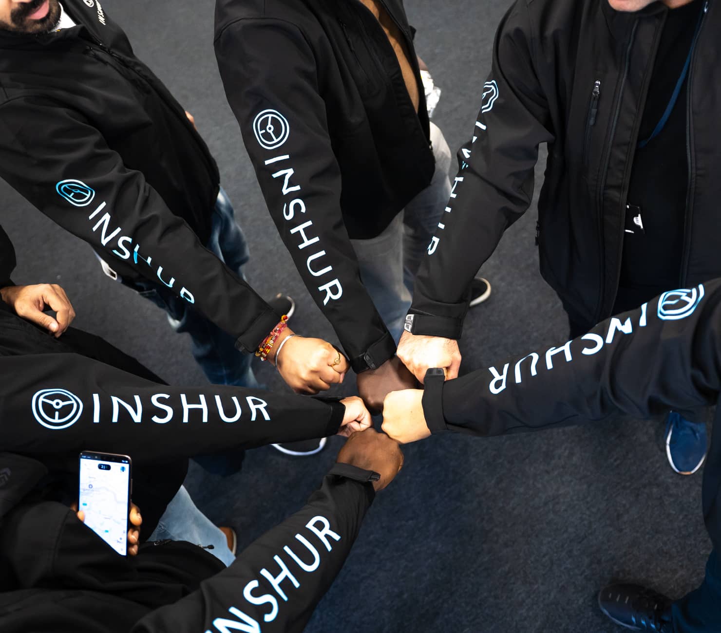 INSHUR employees wearing branded black hoodies gather their fists in a circle