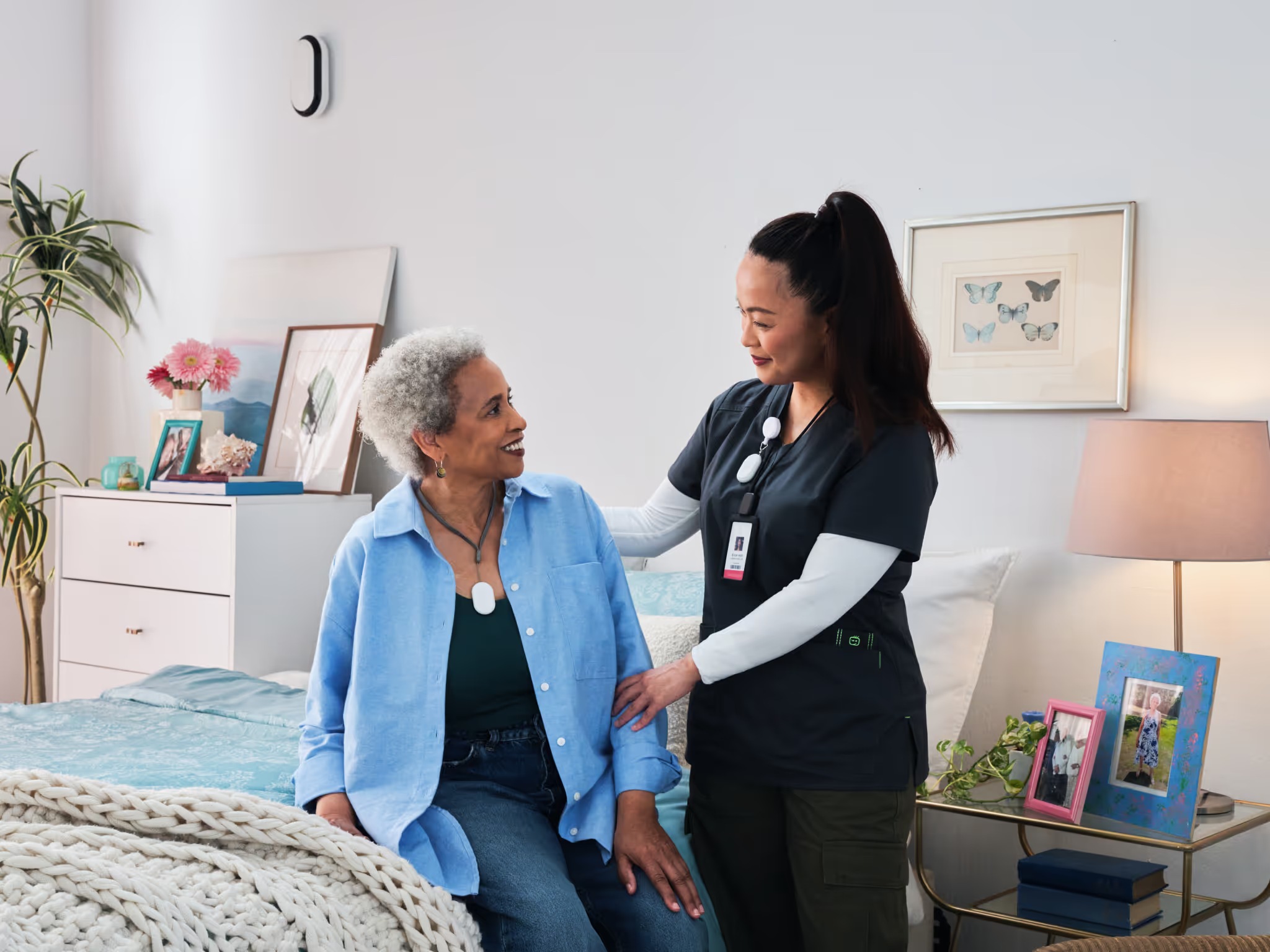 A caregiver beside a resident in a bedroom, with an Inspiren device mounted on the wall
