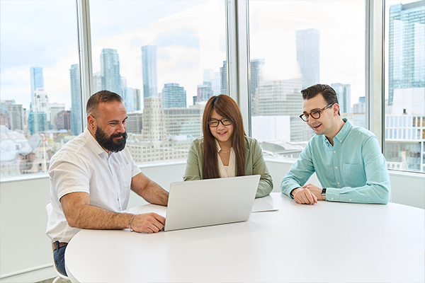 Three Intact colleagues collaborating around a laptop in a bright office