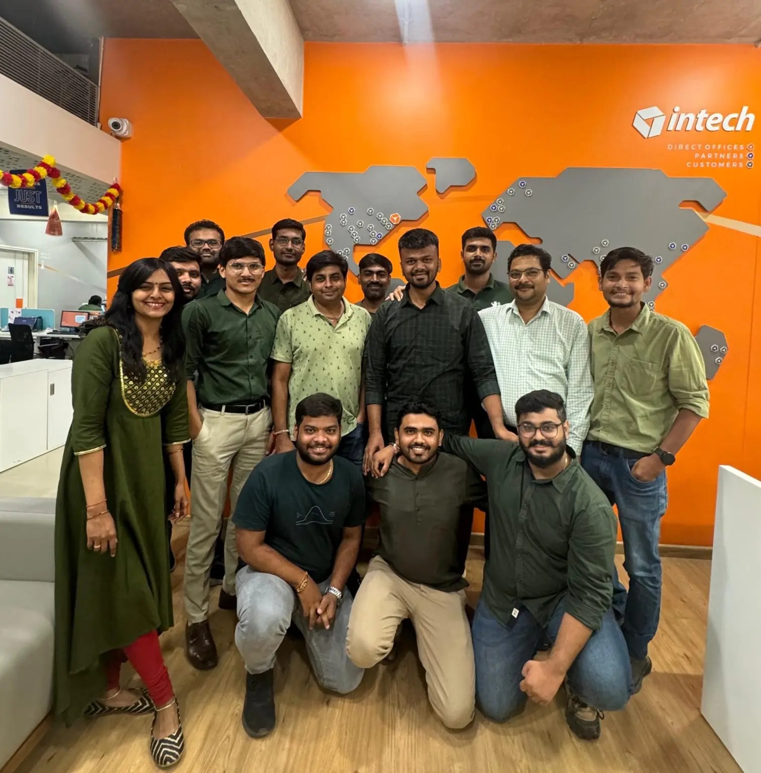 Intech colleagues together in an office with an orange wall and world map