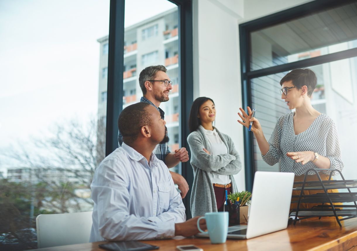 Four people in a bright office discussing work around a laptop