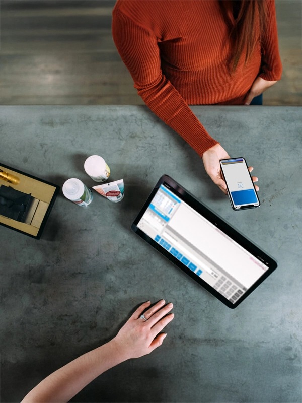 Overhead promotional photograph of a shopper holding a phone beside a retail touchscreen