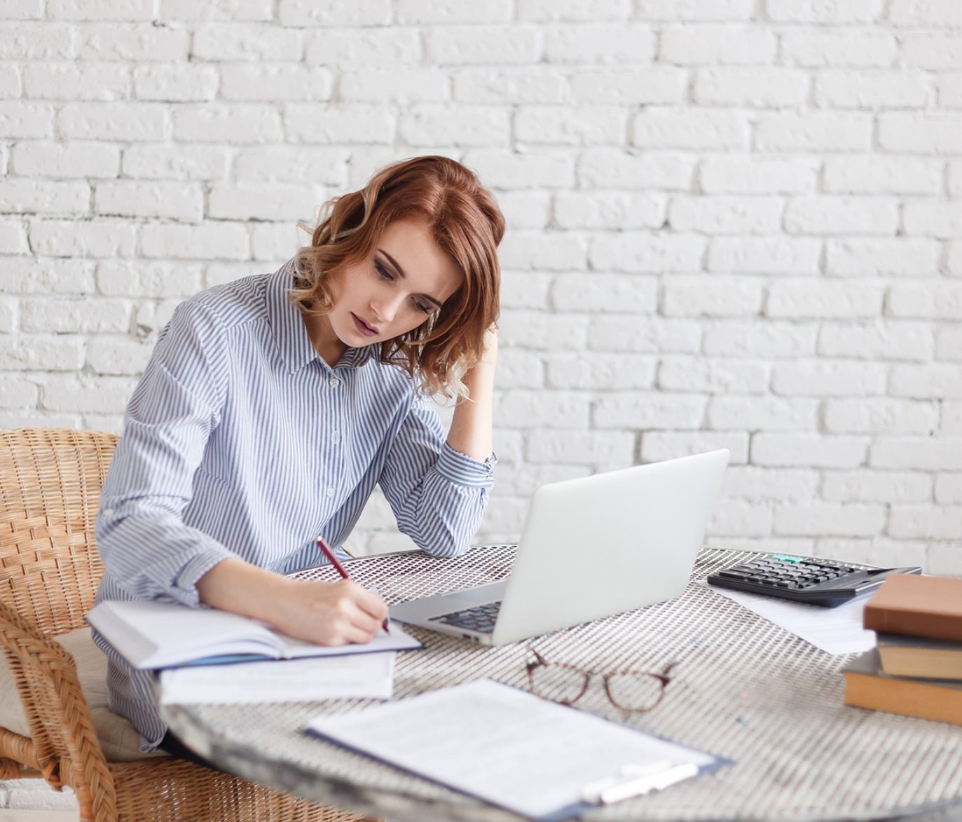 A woman reviewing paperwork beside a laptop and calculator