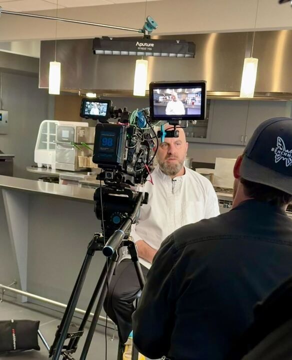 A camera crew filming a chef in a commercial kitchen