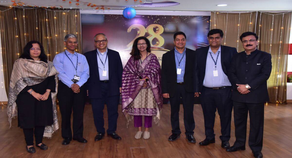 Seven people pose at an InterraIT annual-day celebration beneath a 28th-anniversary backdrop