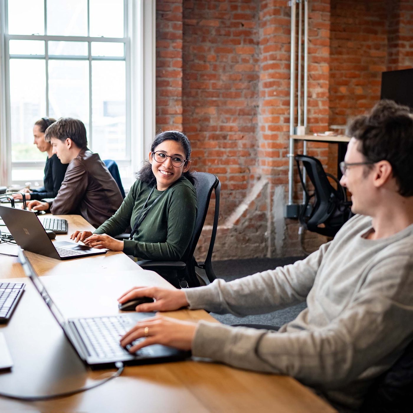 Intersect colleagues working together at laptops in a brick-walled office