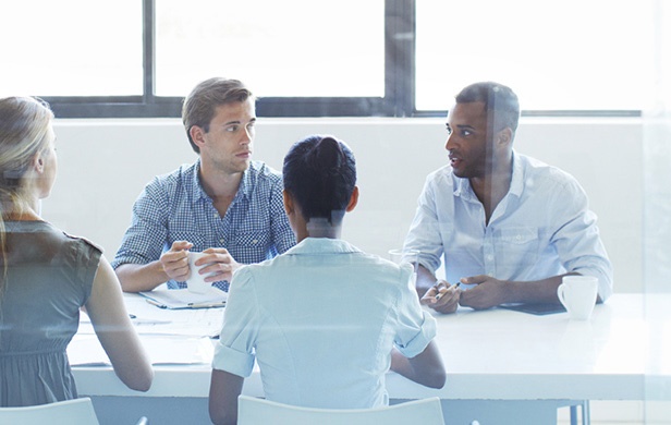 Four businesspeople discussing work around a meeting table in an illustrative case-study photograph