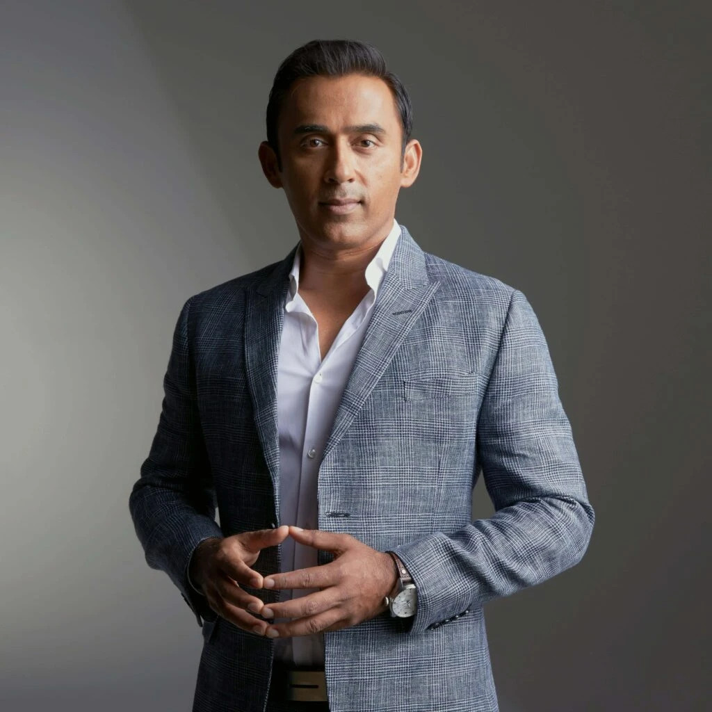 Irfan Khan standing in a checked suit against a gray studio background