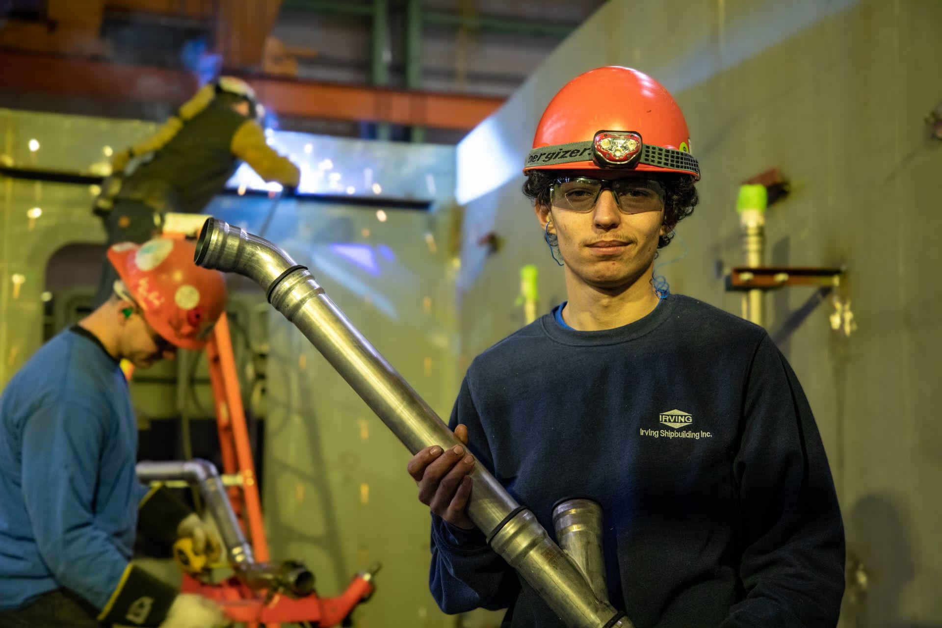 An Irving Shipbuilding tradesperson holding a fabricated pipe section inside Halifax Shipyard