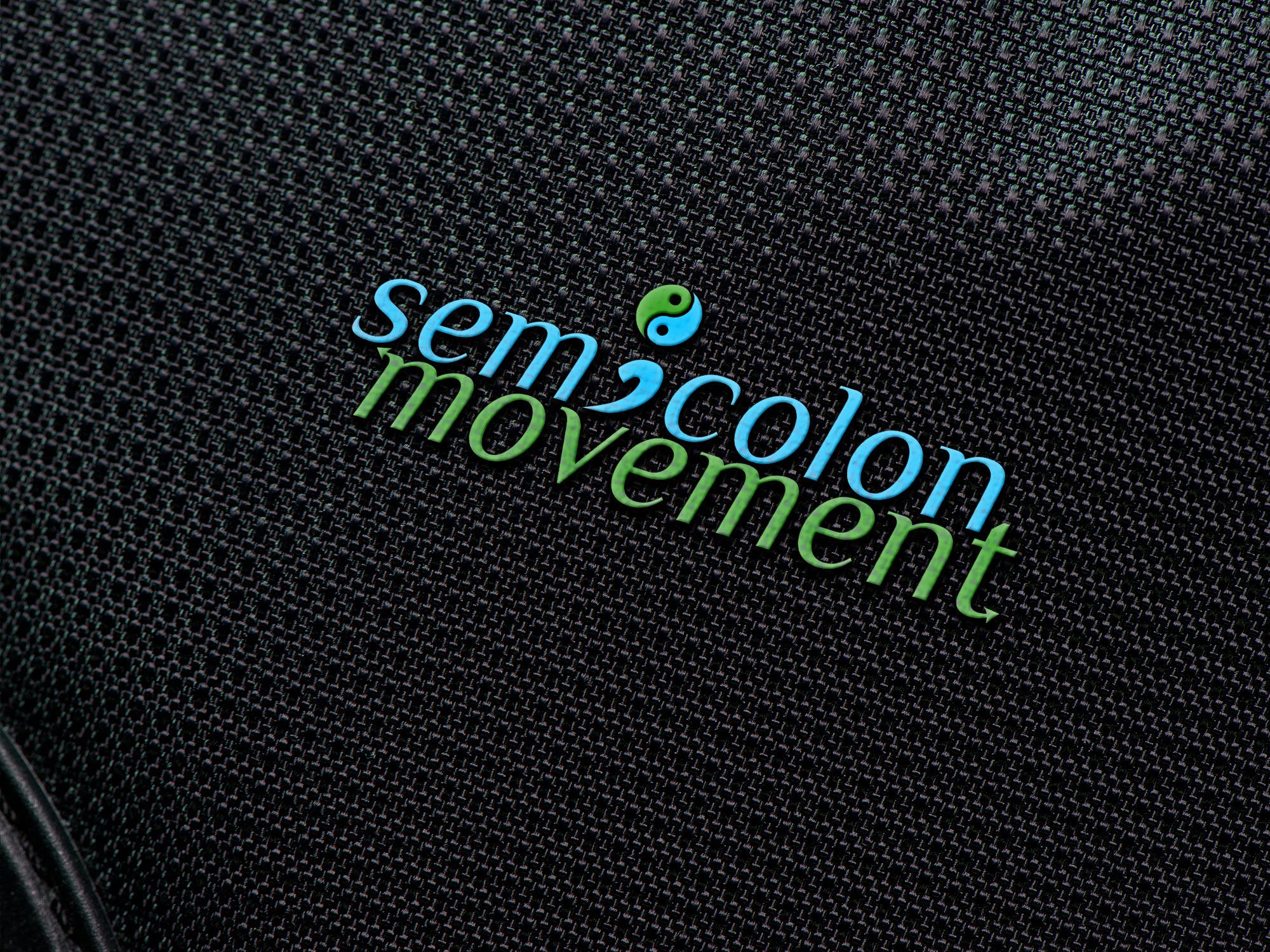 Semi colon movement logo in blue and green on a dark textured fabric mockup from Hossain’s freelance portfolio