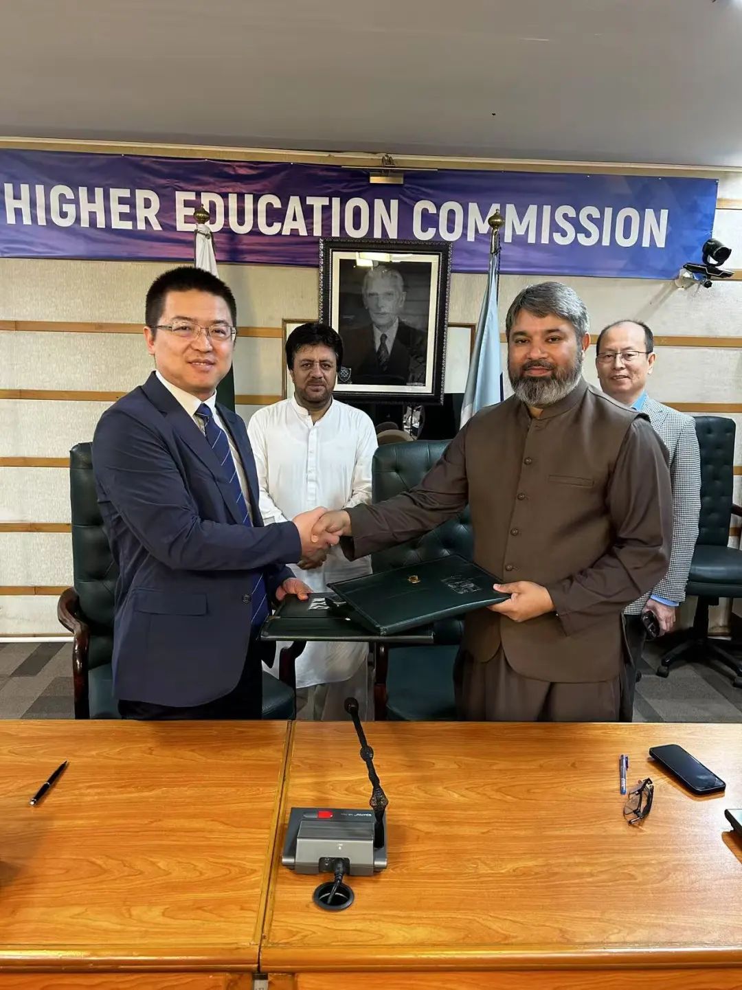 Representatives shake hands and hold documents at Pakistan’s Higher Education Commission