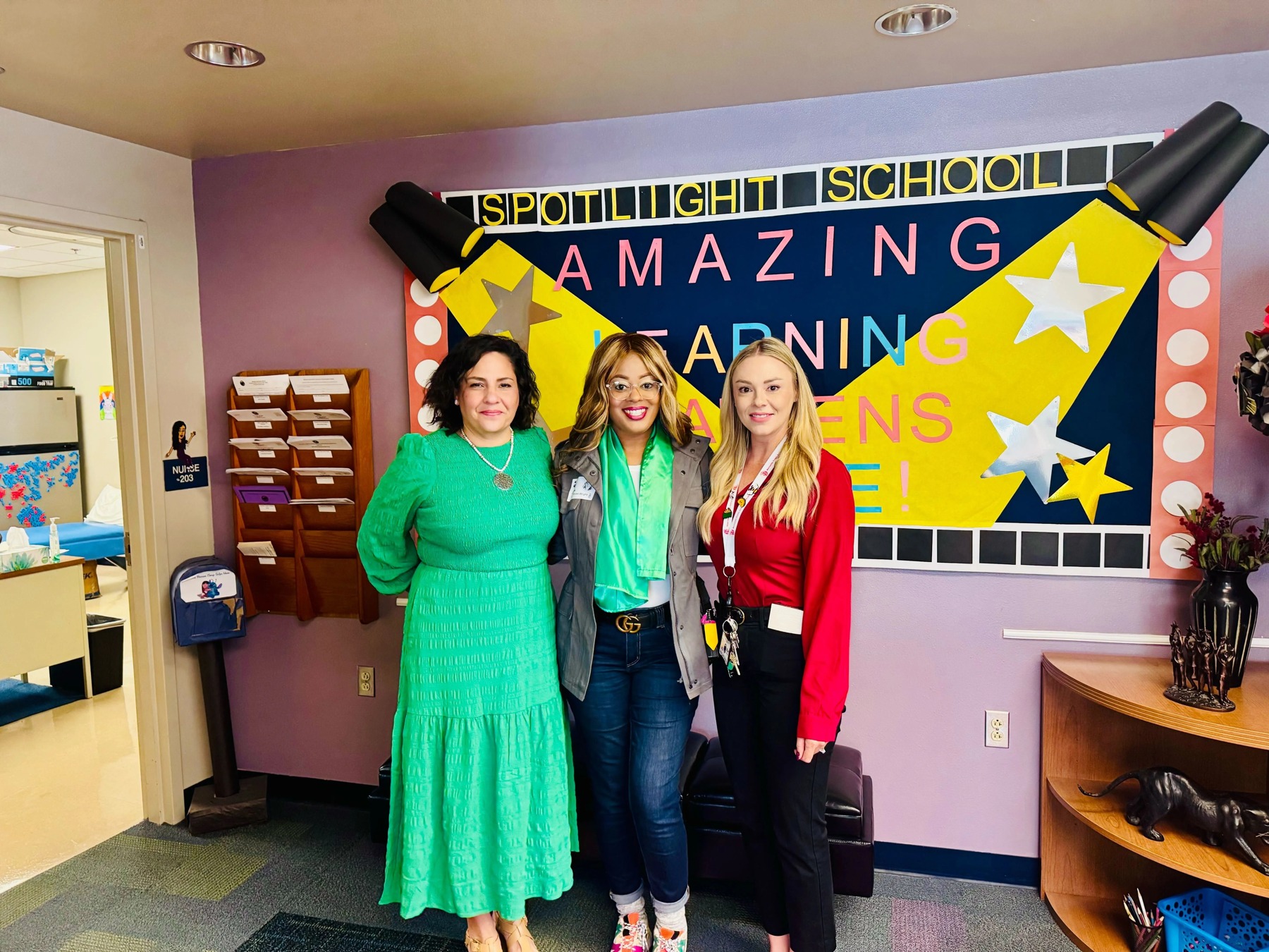 Three adults at a school beneath a colorful Spotlight School bulletin board, in a photo published by Amira Learning