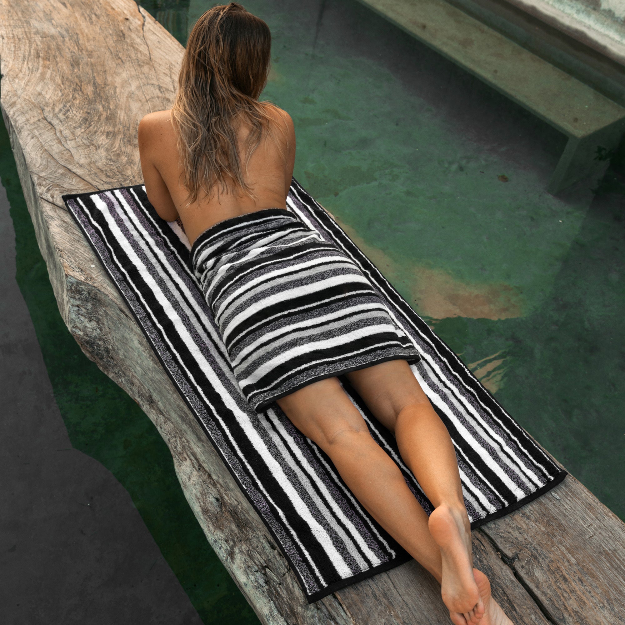 A person reclining outdoors on an Italic striped cotton bath sheet