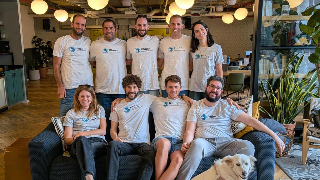 Rhino colleagues gather around a blue sofa in an office, with a dog in the foreground