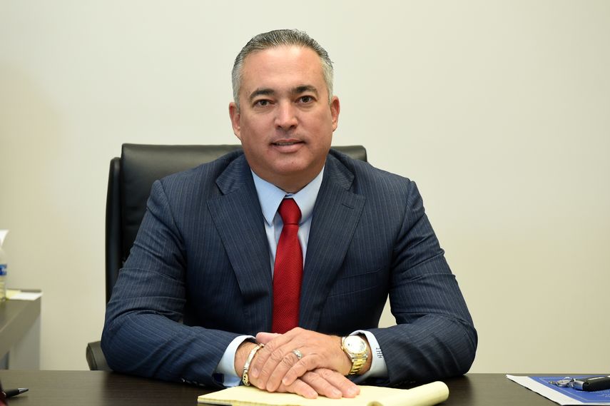Ivan Herrera seated at his office desk in a dark suit and red tie