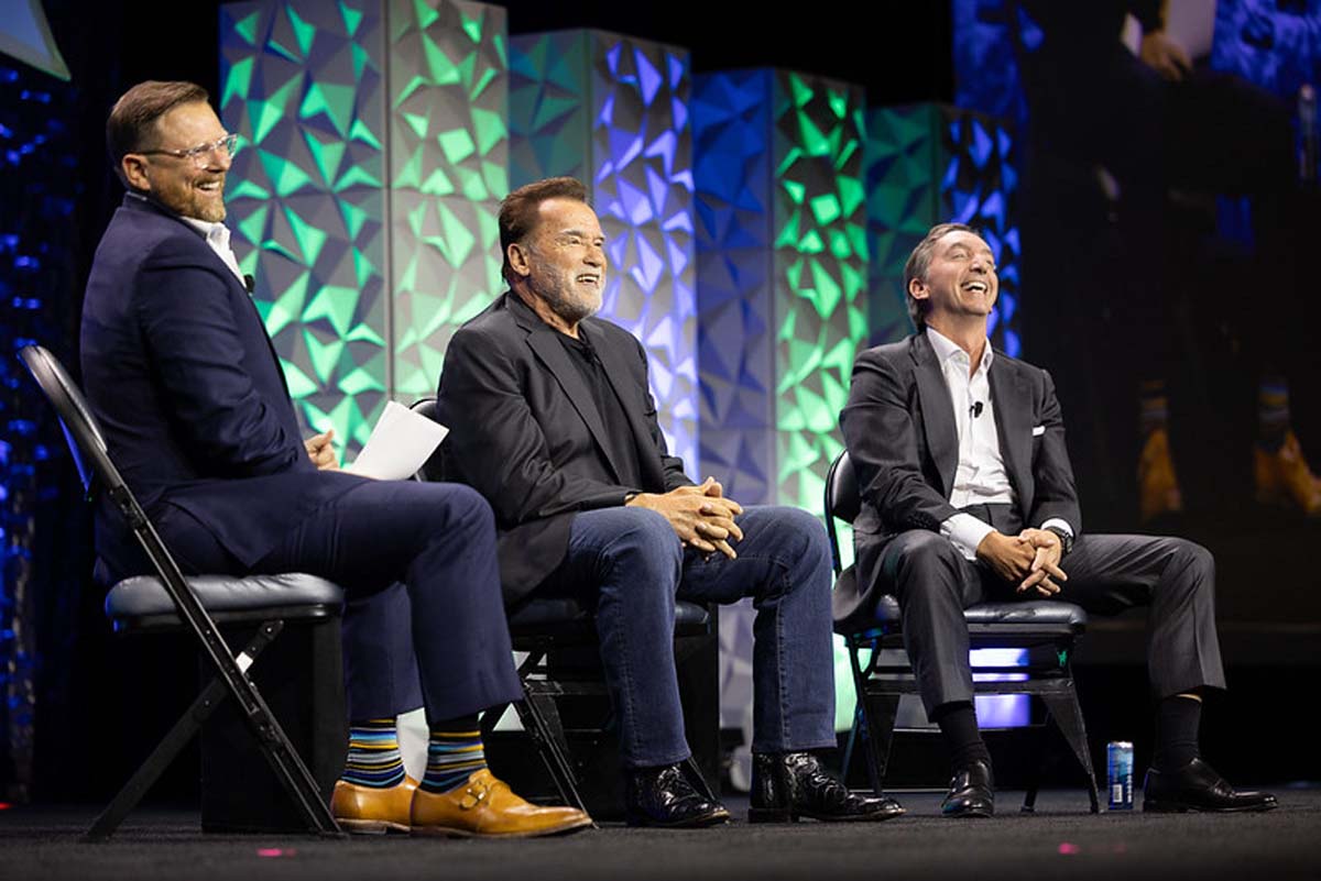 Scott Whitaker, Arnold Schwarzenegger and Ivan Tornos laughing together on a conference stage
