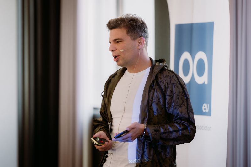 Ivan Zhiznevsky speaking at a Payments Association EU conference in Lisbon, wearing a patterned jacket and headset microphone
