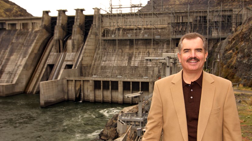 J. LaMont Keen in a tan jacket standing beside a hydroelectric dam