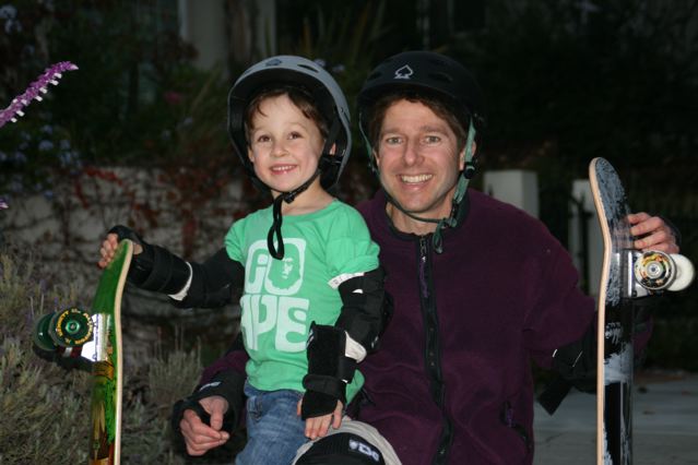Jack Herrick and a child wearing helmets and holding skateboards
