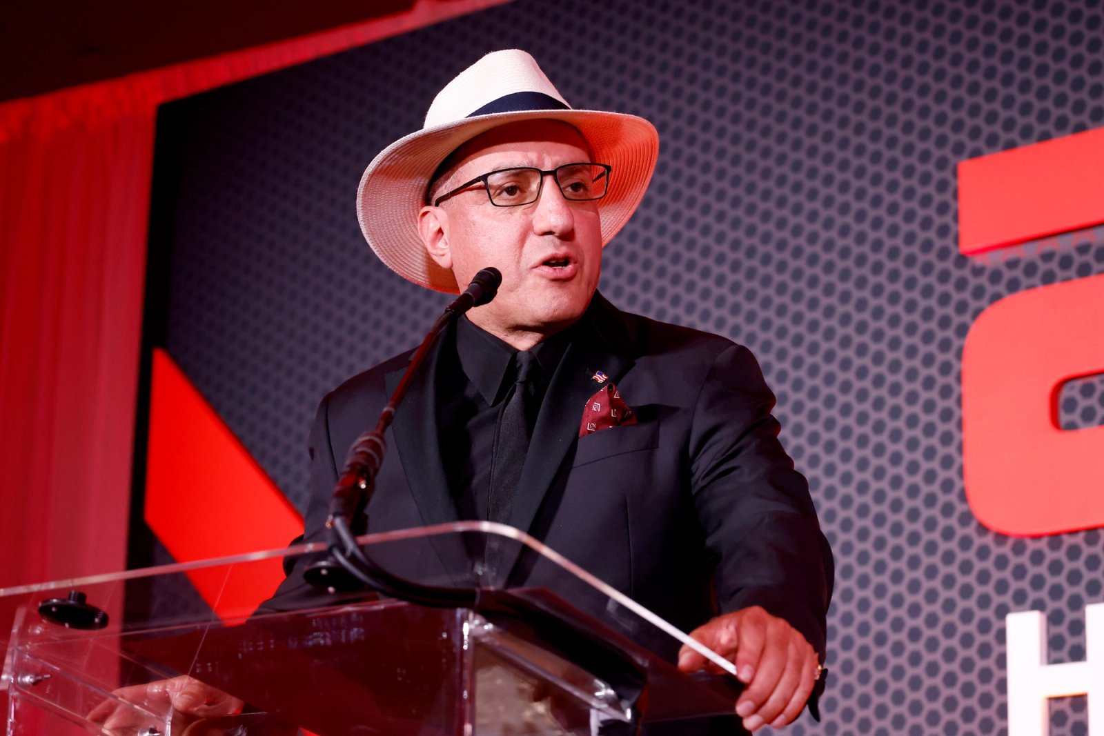 Jack Hidary speaking at a public event in a dark suit and light hat